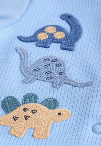 Tessuto a coste azzurro chiaro con tre dinosauri ricamati in blu navy, grigio e marrone, dotati di dettagli distintivi come macchie e cuori.