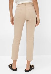 Beige cropped broek met een slim fit, voorzien van twee achterzakken, gemaakt van een zacht materiaal. Gedragen met zwarte sandalen en lichte blootstelling van de enkels.