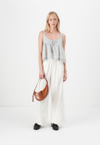 Lichtgrijze mouwloze top met kantaccenten, losse witte broek en een bruine handtas met krokodilprint in een gebogen vorm. Zwarte schoenen.