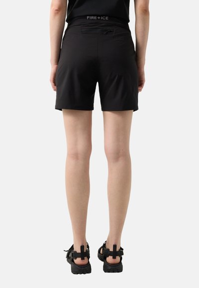 Rückansicht einer Person, die schwarze Shorts mit einer Reißverschlusstasche und schwarze Outdoor-Sandalen trägt, stehend vor einem einfachen Hintergrund.