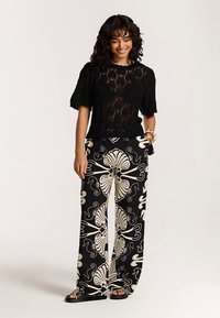 Črna čipkasta majica s kratkimi rokavi, kombinirana s širokimi hlačami z velikim kremnim cvetličnim vzorcem na črni podlagi.