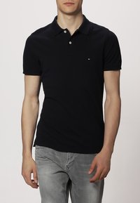 Granatowa koszulka polo z krótkimi rękawami, dwukolorowym plisowaniem oraz małym logo na piersi. Wykonana z bawełny, o klasycznym kroju.