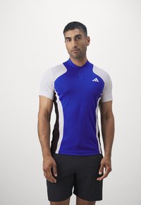 Blauwe sportshirt met korte mouwen, witte en zwarte zijpanelen, en een kwart rits. Voorzien van het Adidas-logo op de borst en een gestructureerde stof.