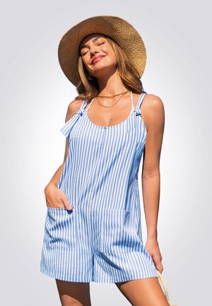 Salopette rayée bleue et blanche avec des poches, en tissu léger. Les bretelles sont nouées sur les épaules et la coupe est ample, portée avec un chapeau en paille.
