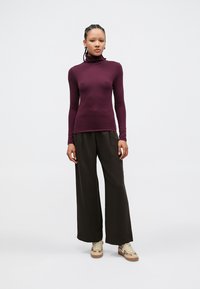 Fitted maroon turtleneck sweater with long sleeves paired with wide-leg olive green pants and light brown sneakers. Minimalistic design.