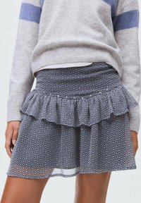 Vijolična kratka krila s krožnim robom, ki ima geometrijski vzorec. Izdelana iz lahkega materiala z gladkim zaključkom.