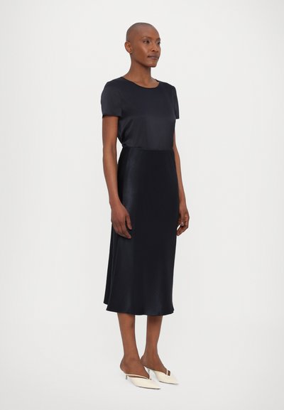 Temno modra obleka s svilen zgornjim delom in kratkimi rokavi ter satenastim krilom. Tokratna silhueta, gladka površina, v kombinaciji s svetlimi sandali na peto.