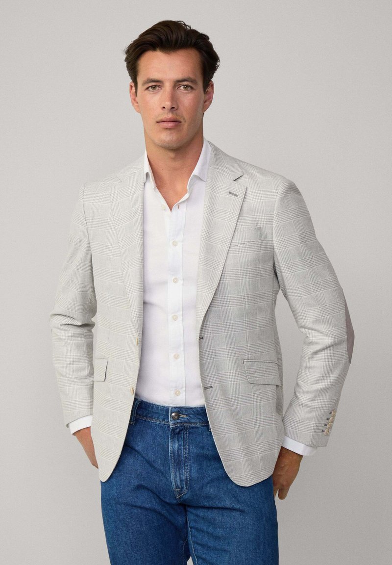 Blazer checked grigio chiaro con chiusura a due bottoni, rever a scomparsa e tasche a toppa, abbinato a una camicia bianca e jeans blu.