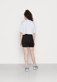 T-shirt curta, cinza claro, com mangas largas, combinada com uma saia preta curta e ténis azuis. Fundo liso.