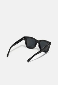 Black sunglasses with a glossy finish, cat-eye shape, and polarized dark lenses. Features silver hardware and the brand “QUAY” on the temples.