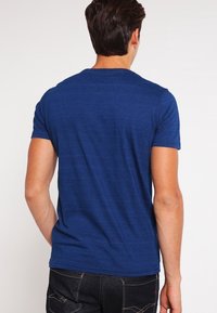 Námořnická modrá trička s krátkým rukávem vyrobená z hladké tkaniny, s kulatým výstřihem a jemnou melírovanou texturou na zadní straně.