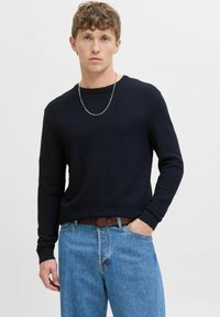 Pull en maille côtelée bleu marine foncé avec un col rond, des manches longues et une coupe décontractée, associé à un jean bleu clair et une ceinture marron.