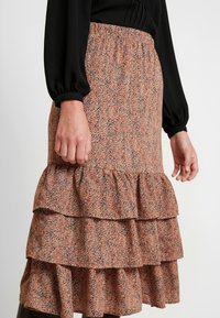 Jupe midi à motif floral dans des tons terreux, présentée avec un design à volants superposés et une taille froncée pour un ajustement réglable.