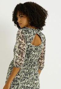Vestido estampado en un tejido ligero y transparente que presenta un diseño ikat en verde y negro. Detalle de ojal en la parte posterior y mangas de tres cuartos.