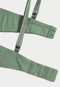 Reggiseno verde con spalline regolabili e chiusura a gancio. Tessuto morbido e liscio con finitura opaca, dotato di cuciture piatte e senza decorazioni.