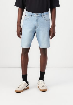 Ljusblå denimshorts med rak skärning, fållade kanter, fem fickor och knäppning, tillsatta med vita och svarta sneakers.