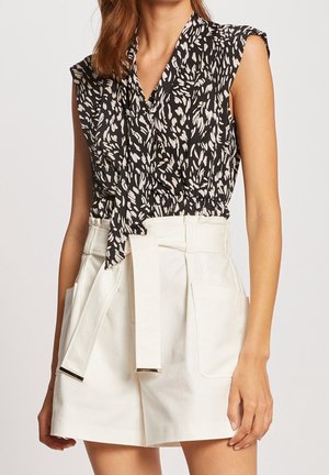 Czarna i kremowa bluzka bez rękawów w kwiatowy wzór, związana w talii, zestawiona z białymi szortami o wysokim stanie z bocznymi kieszeniami.