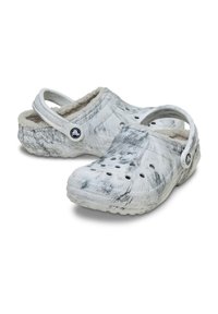 Weiße Holzschuhe mit einem schwarz-grau marmorierten Muster. Hergestellt aus Gummi, mit Belüftungsöffnungen, einem weichen Futter und einem Rückenriemen.