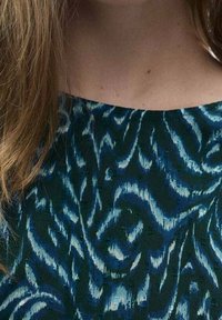 Vestido estampado con un diseño abstracto en azul y verde, con tejido texturizado y un escote ancho, parcialmente cubierto por el cabello.