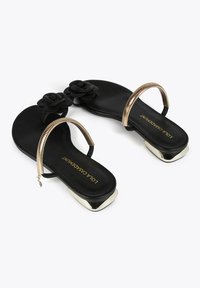 Sandalias negras con adornos florales y una correa metálica dorada con acabado texturizado, punta cuadrada y diseño de tacón bajo.