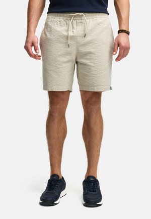Shorts beiges texturés avec une taille élastique et un cordon de serrage. Portés avec des baskets navy. Accent sur un design décontracté et léger.