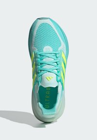 Baskets de sport turquoise avec tige en mesh, rayures jaunes contrastantes et semelle texturée. Présentent un bout arrondi et un système de laçage.