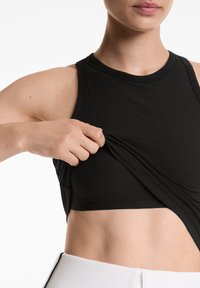 Svart ribbad sport crop top med rund halsringning, som har en tajt passform och en mjuk yta. Modellen justerar tyget vid midjan.