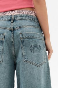 Helle blaue Jeansshorts mit lockerer Passform, ausgestattet mit zwei Gesäßtaschen und einem Logo-Patch. Der Bund weist ein kontrastierendes gemustertes Band auf.