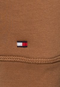 Tessuto di felpa marrone con un piccolo logo ricamato che presenta un design rettangolare rosso, bianco e blu vicino all'orlo.