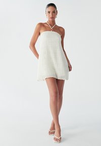 Abito bianco senza spalline con tessuto strutturato e corpetto sagomato, caratterizzato da un collo halter con dettaglio ad anello circolare.