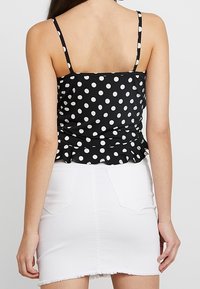 Top peplum a pois bianco e nero con spalline sottili, abbinato a una mini gonna in denim bianco, mostrando il design e i dettagli della textura sul retro.