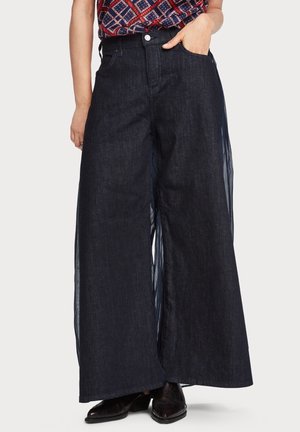 Pantalons palazzo en denim bleu foncé avec des jambes larges et des panneaux latéraux transparents. Dotés d'une fermeture à bouton et de poches. Tissu texturé avec un aspect superposé.