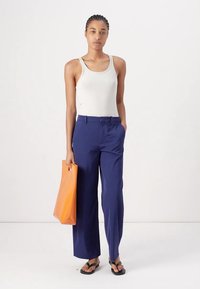 Witte geribde tanktop, marineblauwe wijde broek, zwarte teenslippers en een oranje tote bag. Glad materiaal, casual ontwerp en levendige kleuren.