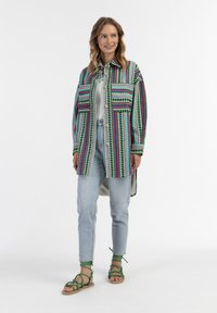 Spalvinga, raštuota ilga palaidinė su žaliais, rožiniais ir mėlynais raštais, derinama su šviesiai mėlynomis džinsomis ir žaliomis sandalais su dirželiais.