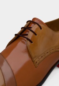 Καφέ δερμάτινο επίσημο παπούτσι με γυαλιστερό φινίρισμα, που διαθέτει καφέ κορδόνια και διακοσμητικές λεπτομέρειες brogue στα πλάγια.