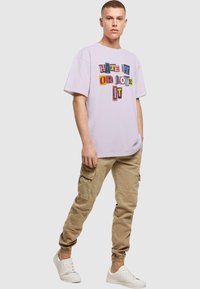 Lavendel kortærmet t-shirt med "HATE IT OR LOVE IT" grafik i farverige blokbogstaver; parret med beige cargo bukser og hvide sneakers.
