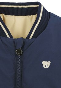 Navyblaue Bomberjacke mit Reißverschluss, geripptem Kragen mit cremefarbenen Streifen und einem kleinen Bärenlogo auf der Brust. Glatte Textur.