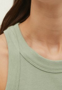 Vihreä uurrettu t-paita, jossa on pehmeä tekstuuri, pyöreä pääntie ja paksut olkaimet, esittelee läheltä kankaan ja ompelun yksityiskohtia.