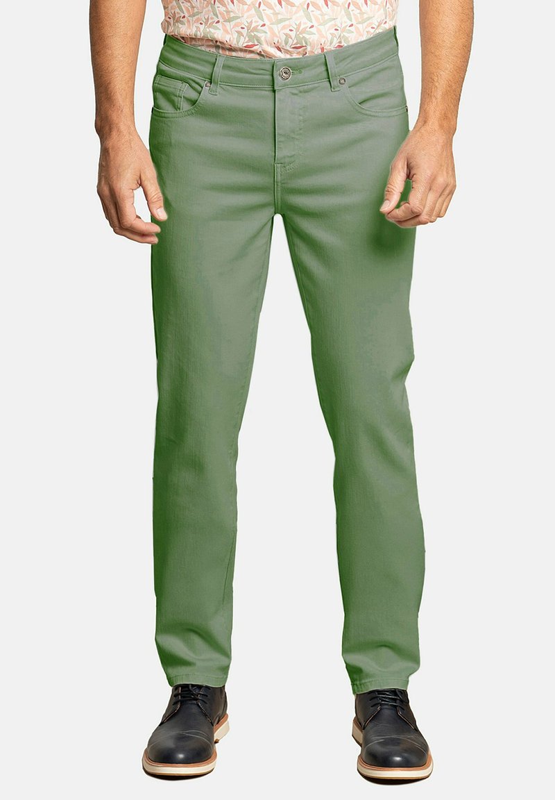 Chinos de algodón verde con un ajuste slim, que cuentan con un diseño clásico de cinco bolsillos, cierre de botón y cintura de media altura. Llevados con zapatos oscuros.