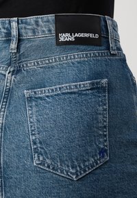 Achteraanzicht van een blauwe denim jeanszak met een zwart label met de tekst "KARL LAGERFELD JEANS" boven de taille.