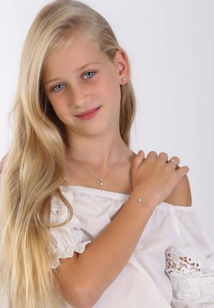 Zilveren sieraden bevatten een hangende ketting, armband en ring met bloemaccenten. Het model heeft lang, steil blond haar en blauwe ogen.