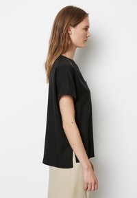 Sort kortærmet t-shirt med en løs pasform, rund halsudskæring, sidelæg og lavet af blødt bomuldsstof. Præsentert mod en neutral baggrund.