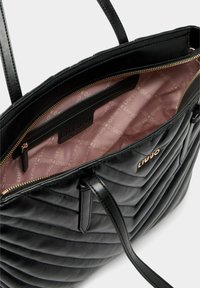 Zwarte doorgestikte shopper met een gladde textuur en een ritssluiting in goudkleur. Het interieur heeft een lichtroze voering en een ritsvak met het label "Liu Jo".