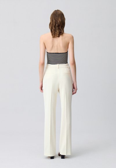 Pantaloni bianchi su misura con una vestibilità dritta, caratterizzati da una texture liscia e dettagli con tasche, abbinati a un top bandeau a righe bianco e nero.