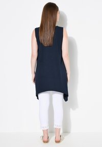 Túnica sin mangas de color azul marino con un dobladillo asimétrico, combinada con leggings blancos que tienen un ribete de encaje en la parte inferior. Ajuste simple y relajado.