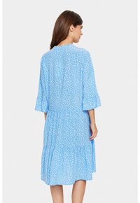 Rochie cu buline albastre, cu mâneci evazate până la trei sferturi, design în straturi, lungime până la genunchi, textură moale a materialului și decolteu rotund.