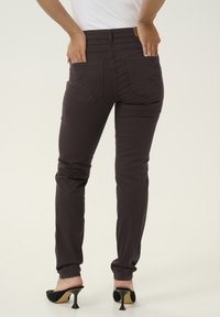 Jeans skinny viola scuro con vita alta, dotati di due tasche posteriori e una texture liscia. Abbinati a scarpe nere con tacco alto.