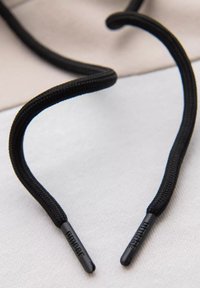 Černé tkaničky s texturovaným, tkaným vzorem, s plastovými koncovkami na obou koncích označenými názvem značky.