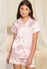 Set di pigiama satinato rosa chiaro composto da maglietta a maniche corte, chiusura con bottoni, una piccola tasca sul petto e pantaloni corti abbinati con dettagli a contrasto.