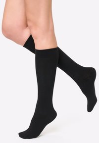 Calcetines de algodón negros hasta la rodilla con una textura suave y puños con canalé, que exhiben un diseño simple y una silueta ajustada.